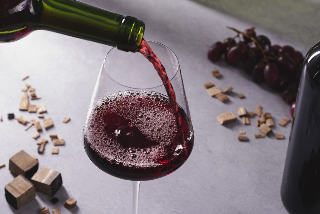 Pouring red wine with oak chips and grapes scattered in the background